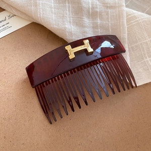 Close-up of tortoise shell hair comb with golden H-shaped metal letter ornament detail