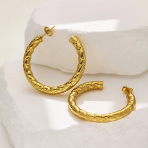 Macro shot of gold hollow earrings featuring an embossed diamond lattice texture on stone