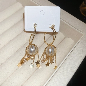 Detail of gold tassel earrings with pearl cage star charms and zircon accents