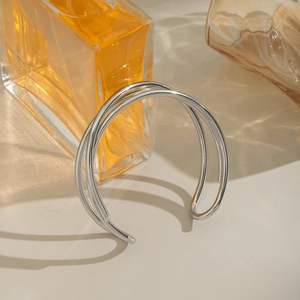 Detail of a minimalist multi-layer crisscross silver metal cuff bracelet on a beige surface