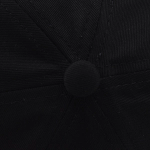 Macro shot of the top button and six-panel stitching on a black cotton baseball cap