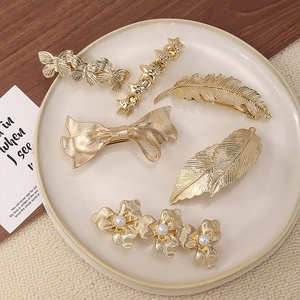 Detailed view of 6-piece gold metal hair clips with butterfly, feather, and pearl floral motifs