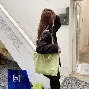 Detalle de bolso de lona verde claro con forro de cuadros morados y correa al hombro