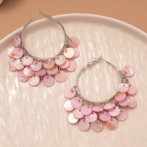 Detail of pink shell disk tassel earrings on a textured ceramic plate in soft light