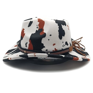 Detail of cow print cowboy hat with brown leather band, gold studs and fringe tassels