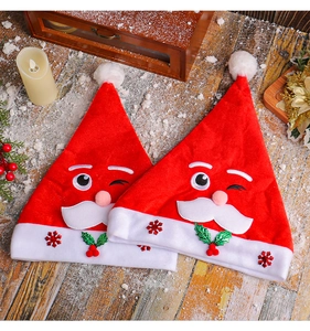 Detail of two plush Santa hats with cartoon faces on a festive snowy wooden surface