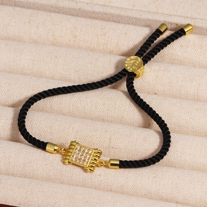 Close-up of black braided cord bracelet with adjustable gold slider and zircon pendant