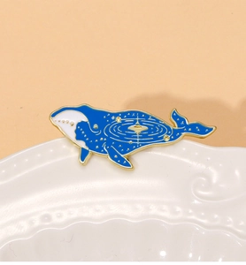 Detailed close-up of blue whale enamel brooch with golden galaxy and star patterns