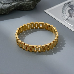 Detailed view of the gold watch-style link bracelet on minimalist dark rocks background
