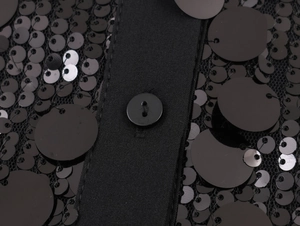 Close-up of black sequins on mesh fabric with a button on a long sleeve party blouse