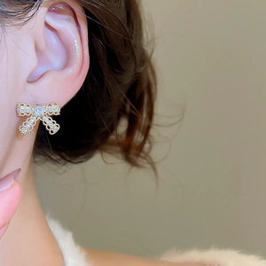 Detailed close-up of a gold-plated bow earring with sparkling cubic zirconia on model ear