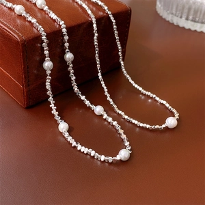 Détail de perles géométriques argentées et perles blanches sur écrin en cuir brun