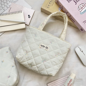 Detailed embroidery of colorful bows on a cream quilted canvas tote bag layout