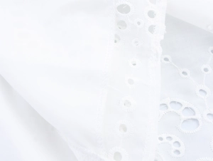 Close-up of white fabric with intricate eyelet embroidery and scalloped edge detail