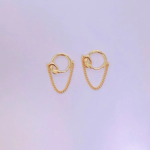 Detail view of gold knot earrings with delicate chain loops on a purple surface