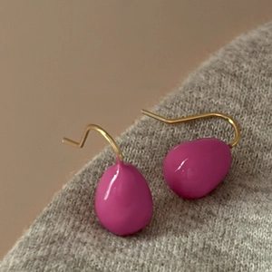 Macro detail of magenta enamel water drop earrings with elegant golden hooks