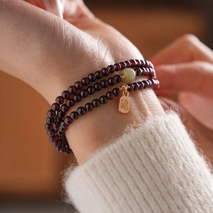 Detailed view of multi-layer garnet bead bracelet with jade and gold Fu pendant on wrist