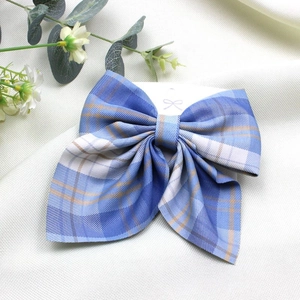 Blue plaid fabric bow hair clip presented on white textured background with eucalyptus