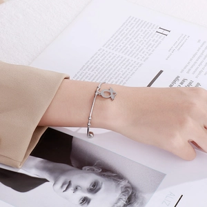 Detailed shot of a minimalist silver stainless steel bangle with a bird charm on a woman's wrist