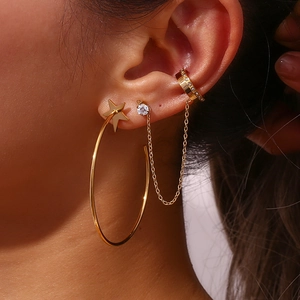 Detail of gold star stud and hoop earrings with chain and rhinestone ear cuff on model