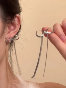Close-up of silver bow earrings featuring long snake chain tassels on a model