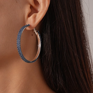 Detail of a model wearing large blue denim fabric round hoop earrings with a silver needle