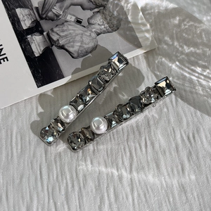 Detailed view of hair clips with dark grey square gems and white pearls on metal base