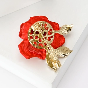 Back view of a red enamel rose brooch with a golden pin on a white platform
