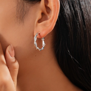 Close-up of a silver twisted hoop earring worn by a model showcasing metallic texture
