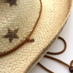 Detail of straw cowboy hat featuring brown star print and adjustable wooden bead strap