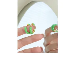 Close-up of green enamel hoop earrings held between fingers with a soft mirror reflection
