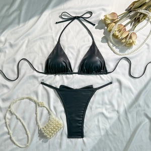 Flat lay of black halter bikini set with shiny metallic texture on white silk backdrop