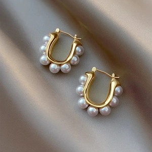 Détail macro de boucles d'oreilles perles dorées en U sur fond en soie de couleur champagne