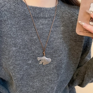 Close-up of a silver ginkgo leaf pendant necklace worn on a dark grey knit sweater