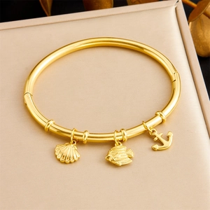 Detailed view of gold bangle with sea-themed charms including shell, fish and anchor