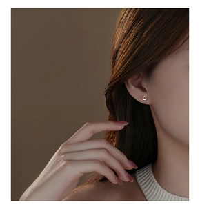 Close-up of a silver teardrop earring on model's ear with soft brown background