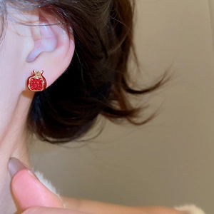 Close-up of elegant red pomegranate stud earring with gold frame on woman's ear
