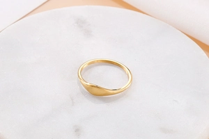 Close-up of minimalist gold titanium ring with high-polish finish on white marble tray