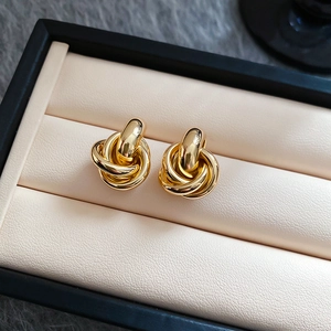 Nahaufnahme goldener geflochtener Metallohrstecker mit Knotendesign in einer Schmuckschatulle