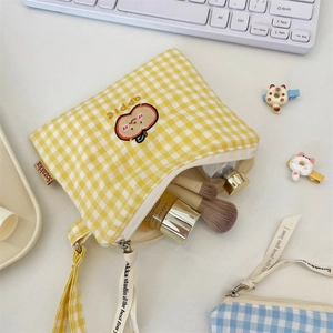 Detailaufnahme der gelb karierten Tasche mit Apfel-Stickerei und Kosmetikartikeln