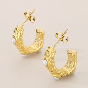 Detail of 18k gold C-shape earrings featuring lava texture and inlaid white pearls