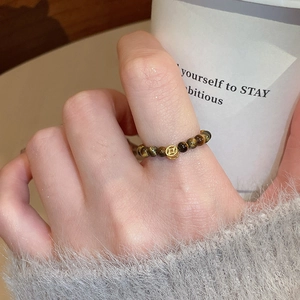 Detail of beaded tiger eye stone ring with a gold hollow charm on a woman's finger