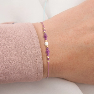 Handmade woven purple cord bracelet with natural stones and pearl on a female wrist