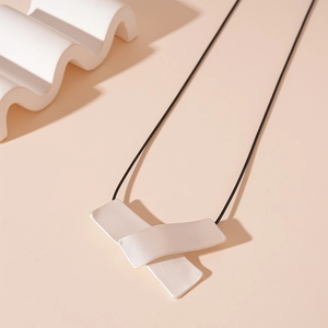 Detail of silver matte geometric pendant with black cord chain on artistic background