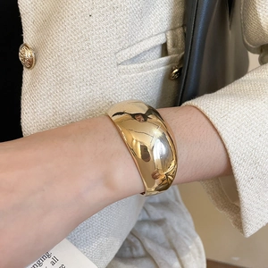 Gros plan d'un bracelet manchette large doré minimaliste avec une finition miroir brillante