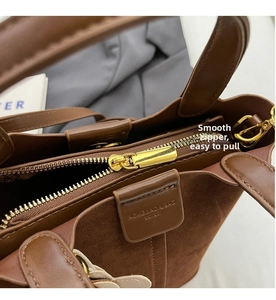 Detailansicht eines goldenen Reißverschlusses und Wildleders auf einer braunen Handtasche