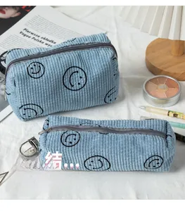 Close-up of light blue corduroy cosmetic bags with black smiley face prints on a desk