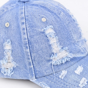 Close-up of distressed light blue denim baseball cap with frayed holes and vintage texture