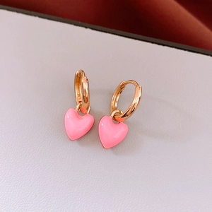 Macro detail of French vintage gold hoops with pink enamel heart charms on white texture