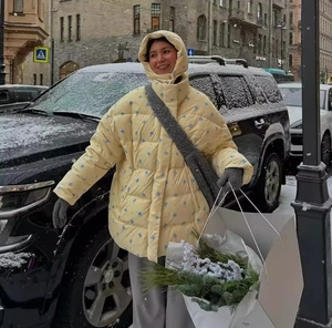 Close-up of a women's yellow hooded puffer jacket with blue floral patterns in winter snow